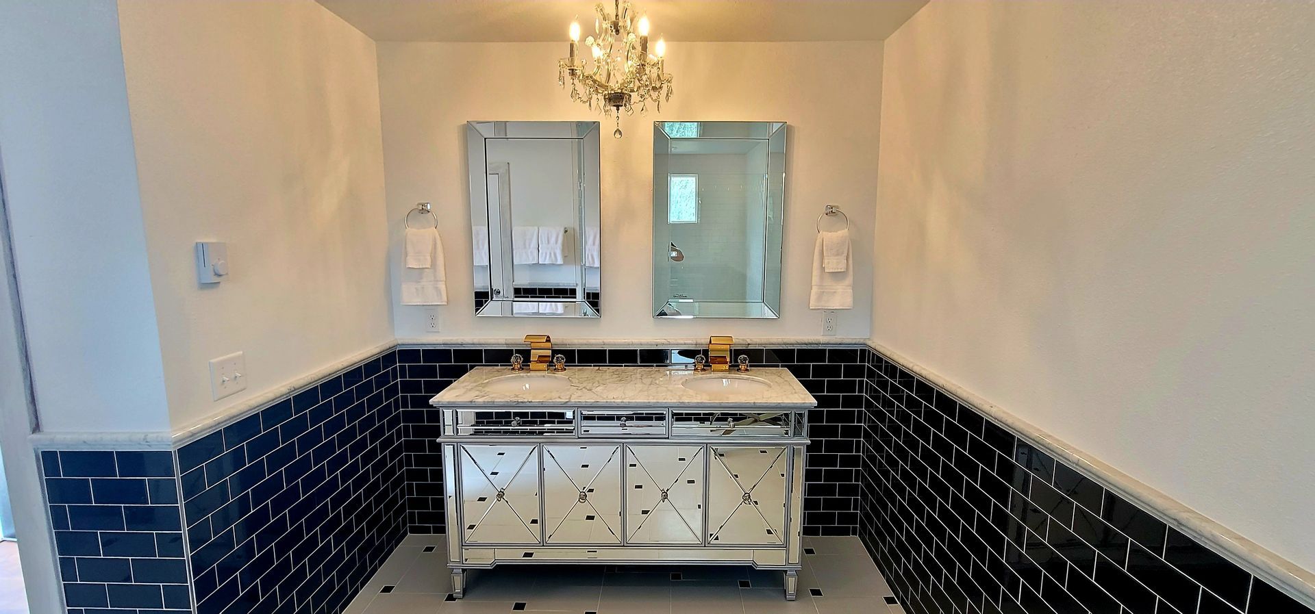 Bathroom with black tile, mirrored vanity, two mirrors, and a chandelier in the Great Gatsby bathroom.