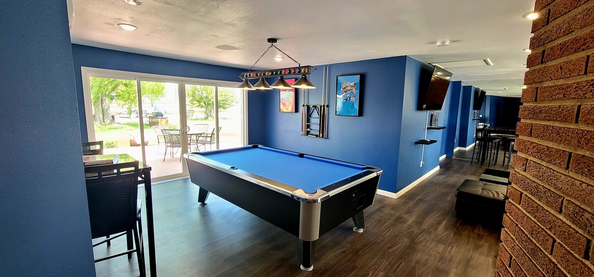 A blue-walled game room featuring a pool table, dark flooring, and a view of an outdoor patio.