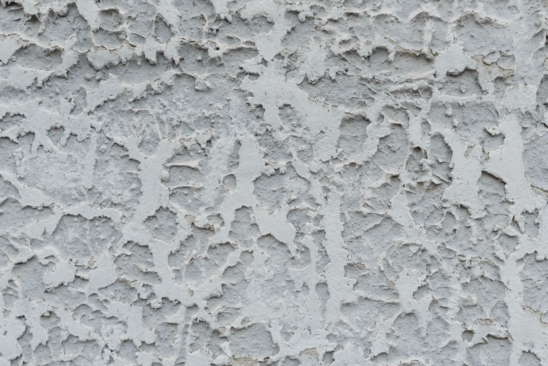 Gray stucco wall with rough, textured surface and irregular white patches
