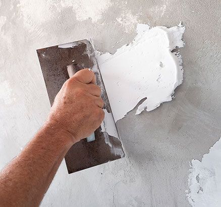 Hand smoothing white plaster over a gray wall with a metal trowel