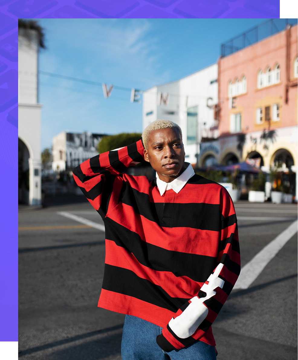 Person in a red-and-black striped sweater posing on a city street with colorful buildings behind.