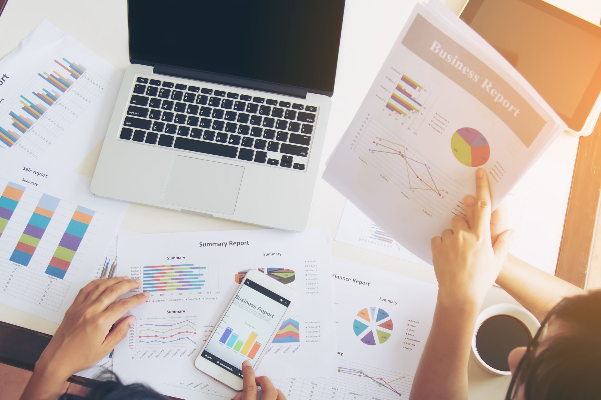 Hands reviewing charts and graphs around a laptop in a bright office setting