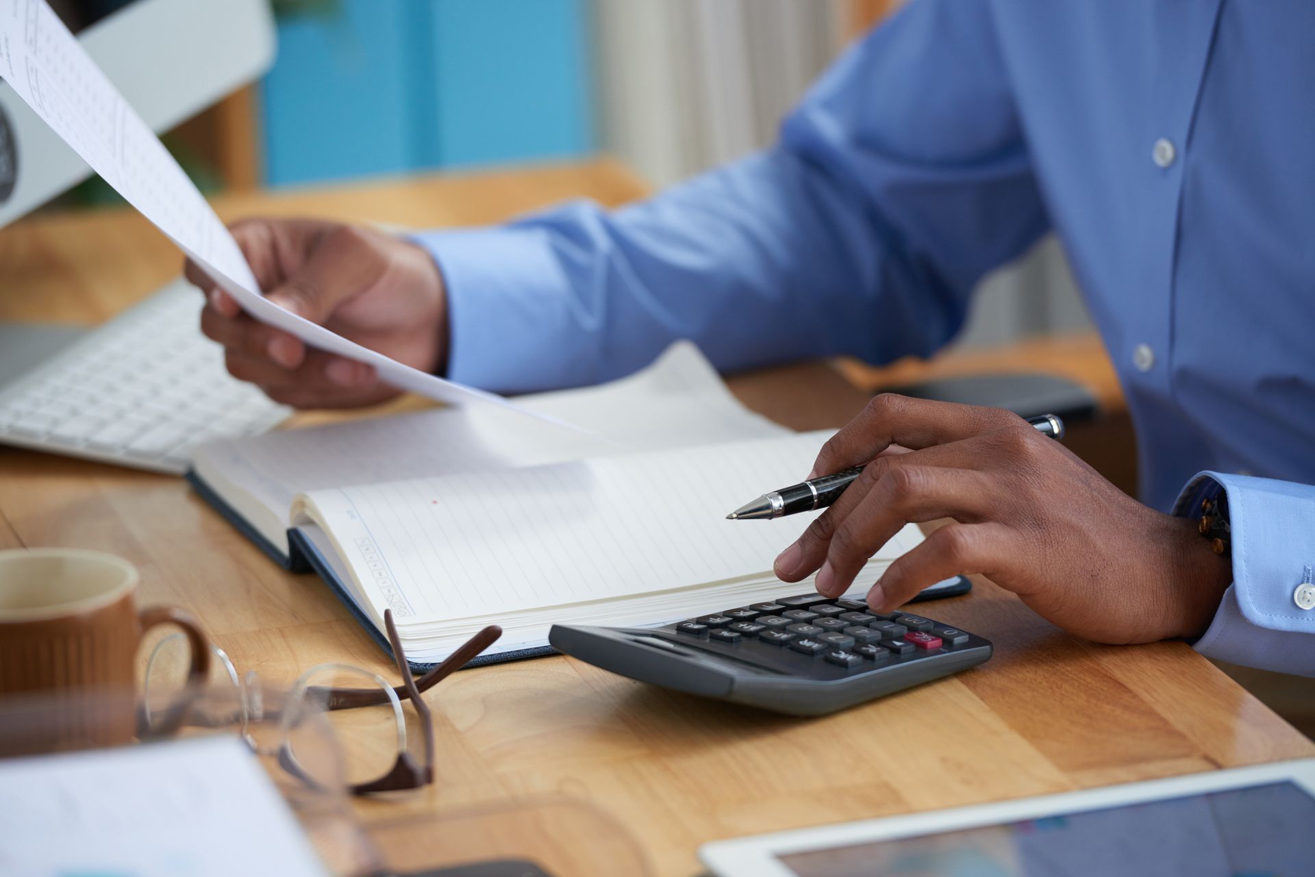 Hands working on paperwork and calculator at a desk with a coffee mug and laptop nearby.