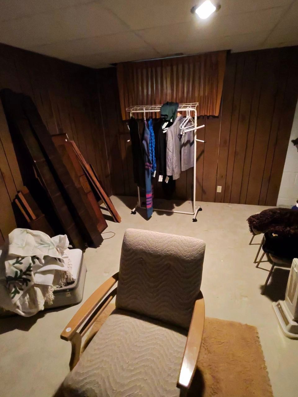 There is a chair in the middle of a room with clothes hanging on racks.