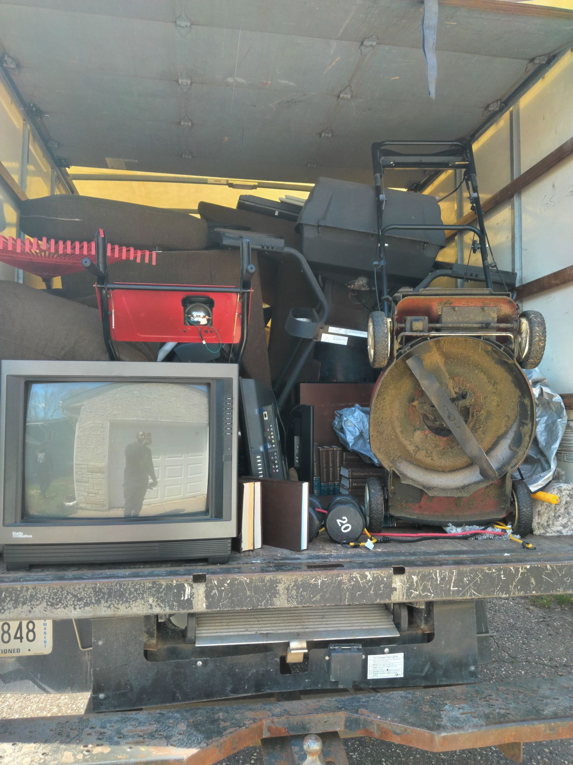 The back of a truck filled with junk including a television and a lawn mower