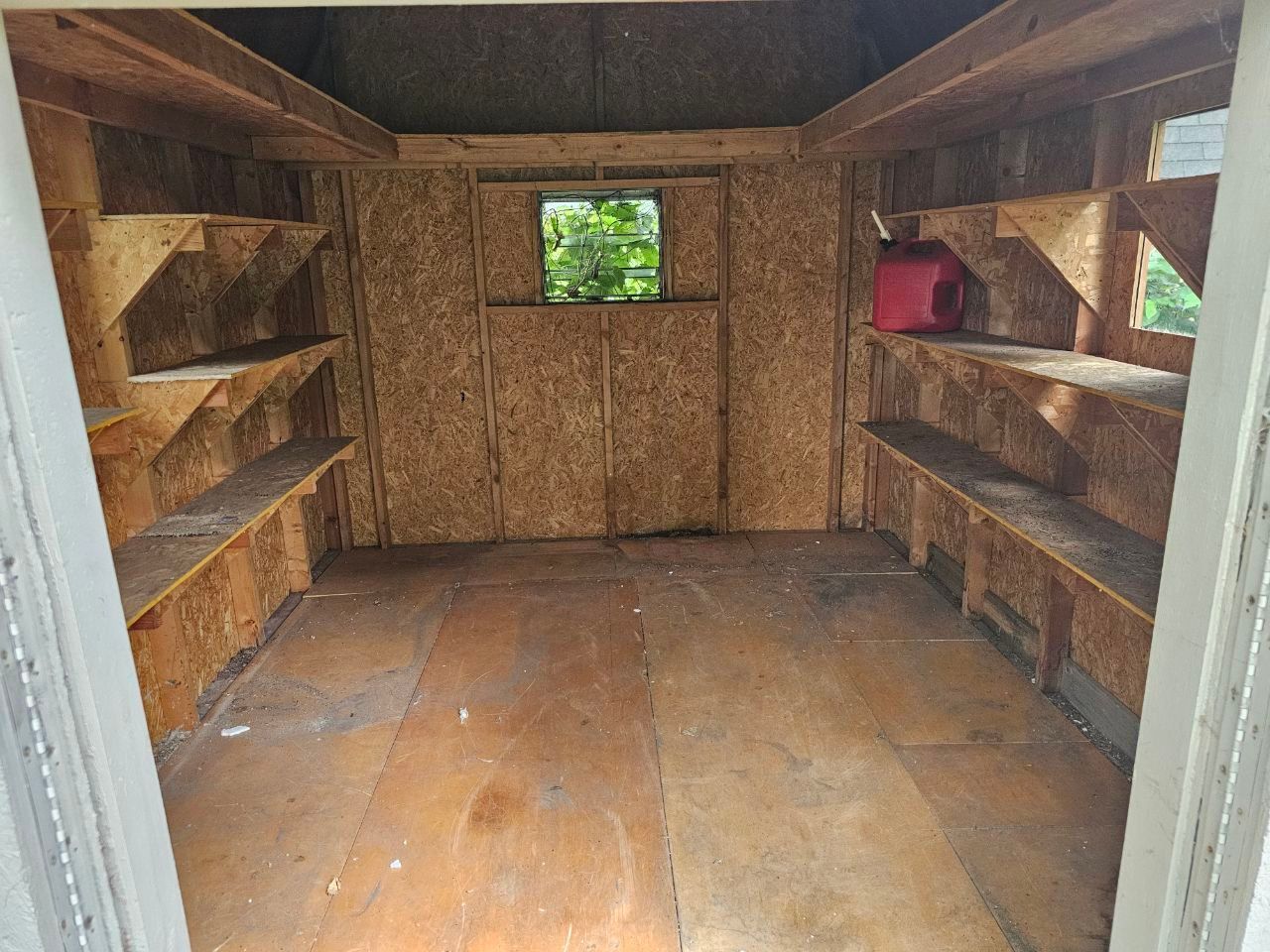 The inside of a wooden shed with shelves and a window.