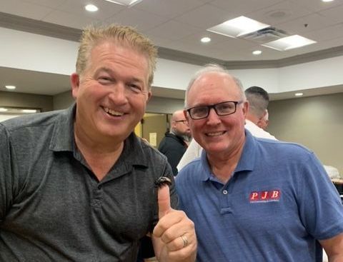 two men are posing for a picture and one of them is giving a thumbs up .