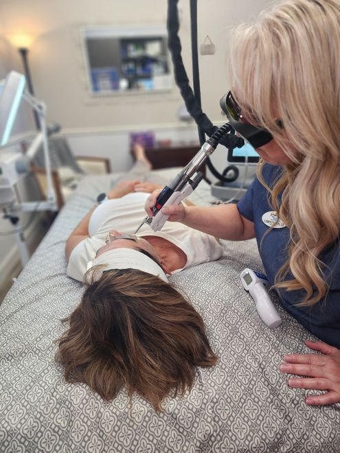 Person getting a facial treatment while a technician uses a tool on their face in a spa room