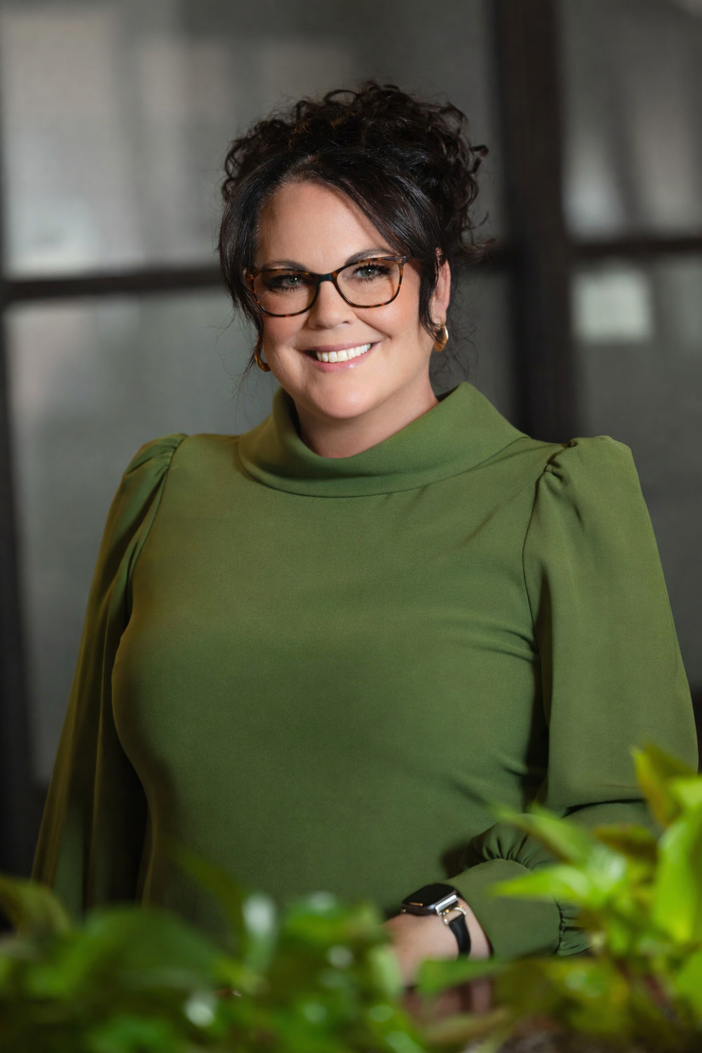 A woman wearing glasses and a blue jacket is smiling for the camera.