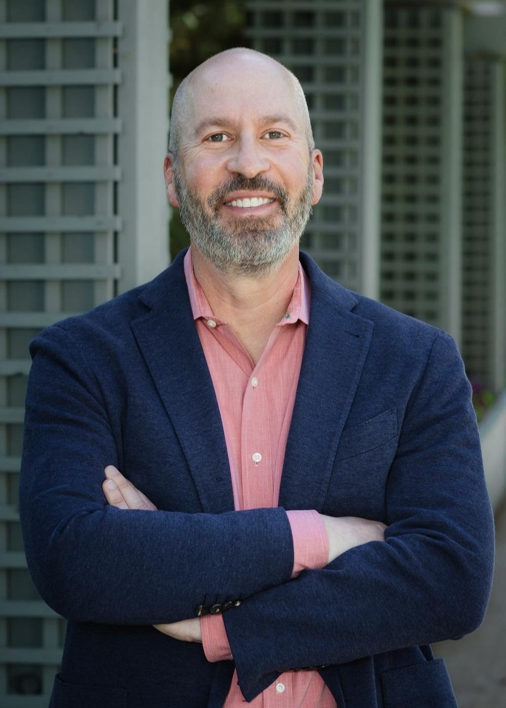 A man with a beard is wearing a blue jacket and a pink shirt.