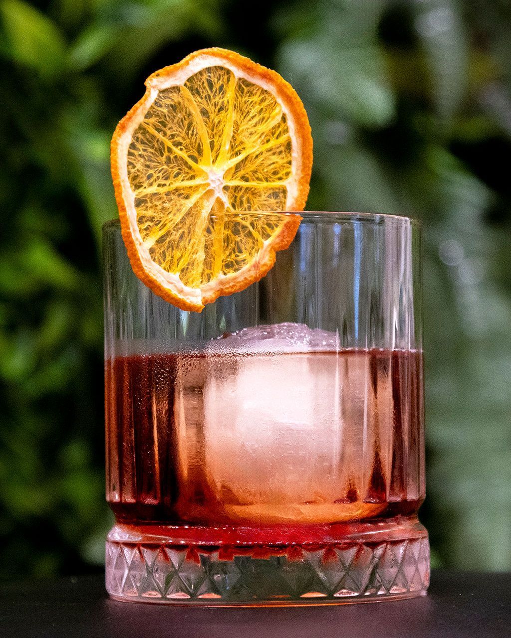 Cocktail with a large ice sphere and dried orange slice garnish.