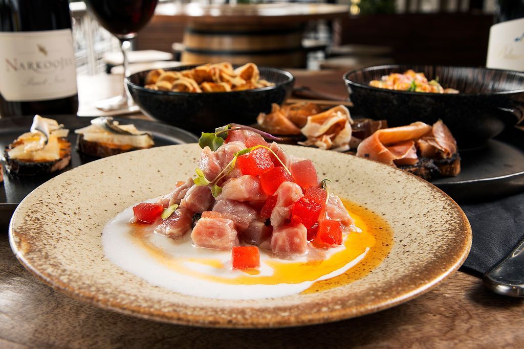 Plate of tuna tartare with surrounding appetizers and wine.