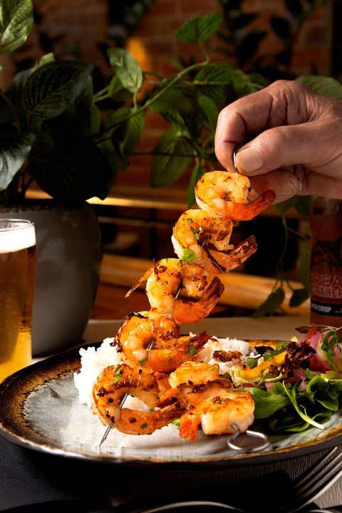 Grilled shrimp skewer over rice and salad, hand reaching to remove a shrimp.