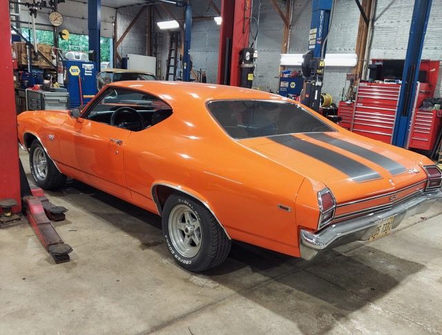 Orange classic muscle car in a garage, viewed from the rear side with gray racing stripes.