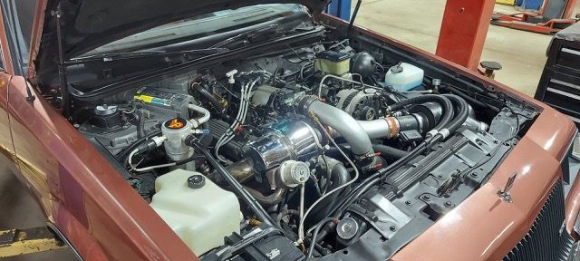 Open car engine bay with a turbocharged setup and exposed components in a garage.
