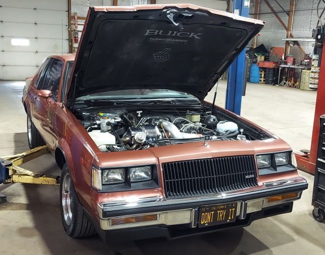 Maroon classic car with hood open in a garage, showing engine bay.