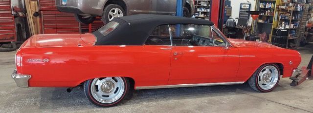 Red classic convertible car with black top in a garage, side view.