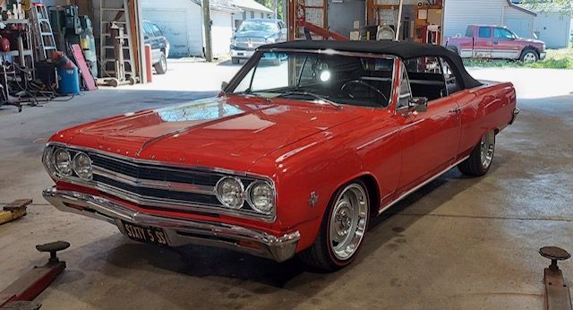 Red classic convertible car in a garage, front-left view, with a black soft top and chrome details