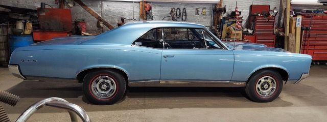 Light blue classic coupe parked in a garage with red wheels and chrome trim
