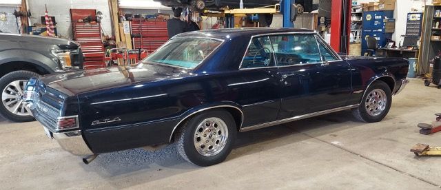 Dark blue classic muscle car in an auto shop garage, shown from the side.