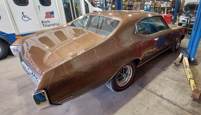 Brown classic muscle car displayed indoors in a workshop or garage, rear three-quarter view