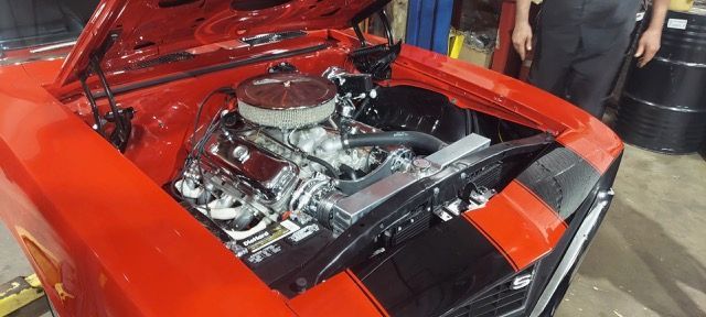 Red classic car with open hood, showing a polished chrome engine in an indoor garage.