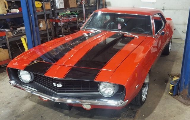 Red classic muscle car with black racing stripes in a garage, front view.
