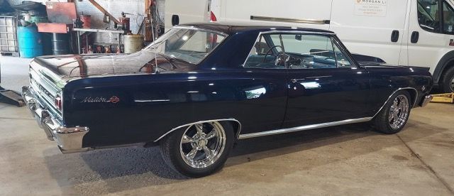Classic dark blue coupe in a garage with a white van in the background