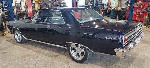Classic black two-door coupe in a garage, side view with chrome trim and custom wheels