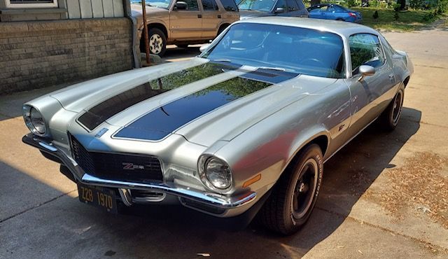 Classic silver muscle car with blue racing stripes parked outdoors on a sunny street