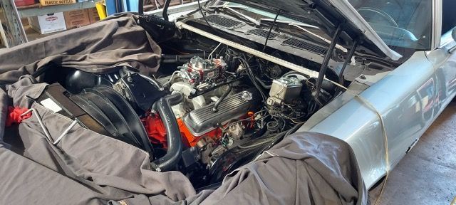 Damaged silver car with hood open, exposing a cluttered engine bay and crumpled front end.