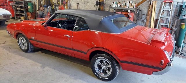 Red classic muscle car with black vinyl roof parked in a garage, side view