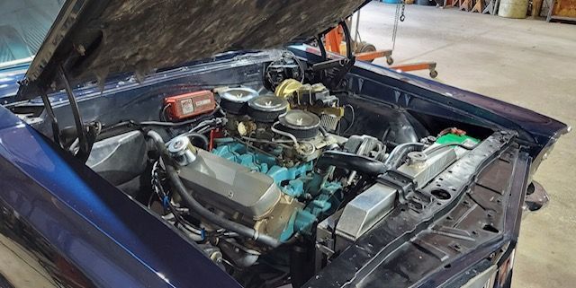 Classic car with hood open, showing a detailed engine bay in a garage.