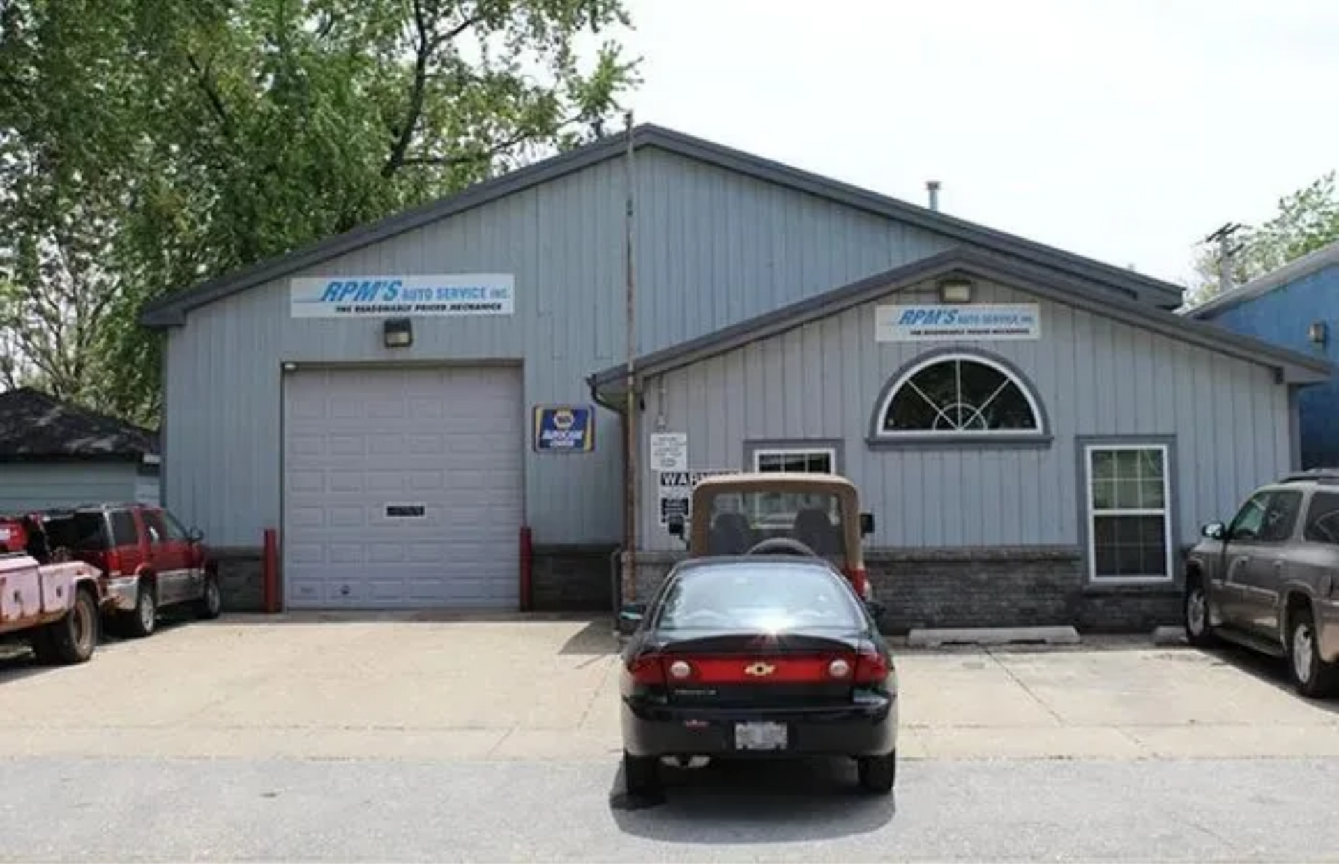 Gray industrial building with parked cars in front and a large garage door