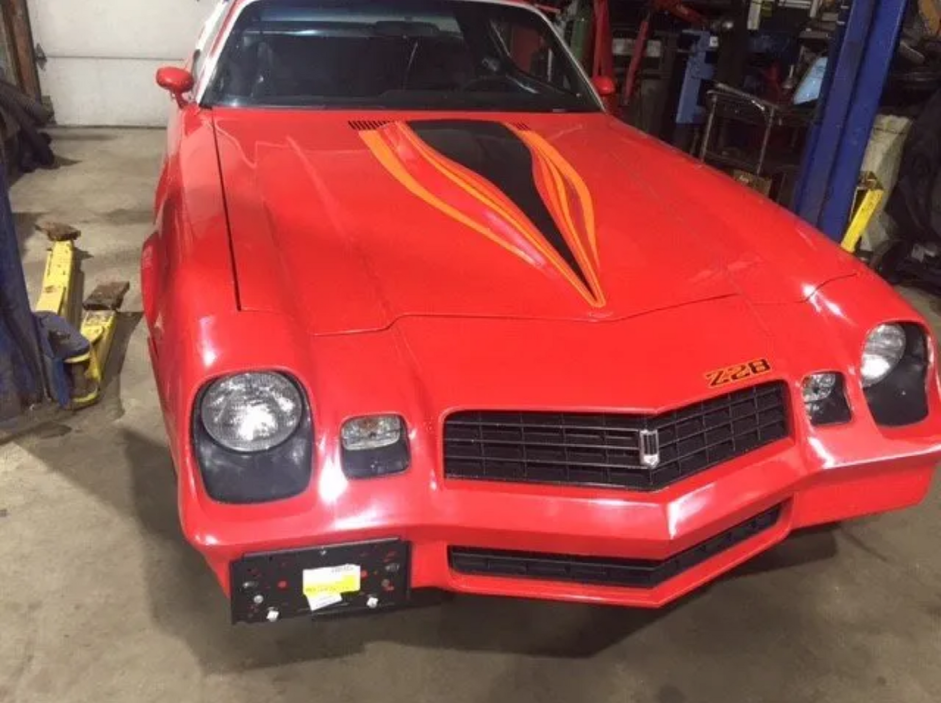 Red vintage sports car in a garage, with black and orange hood flames and a black front bumper.