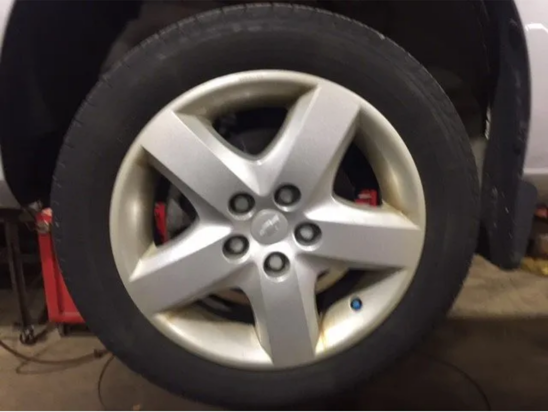 Close-up of a silver car wheel with five spokes and a visible red brake caliper in a garage.