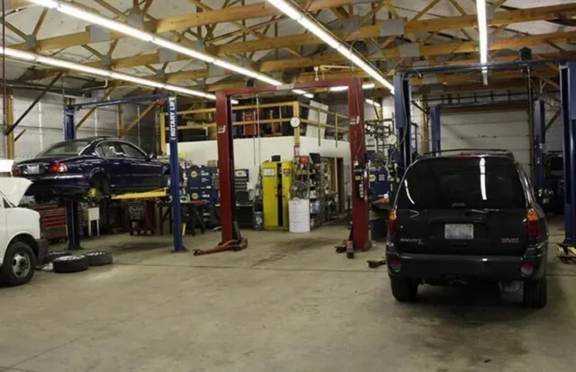 Auto repair shop with cars on lifts, red support posts, and a black SUV in the foreground.