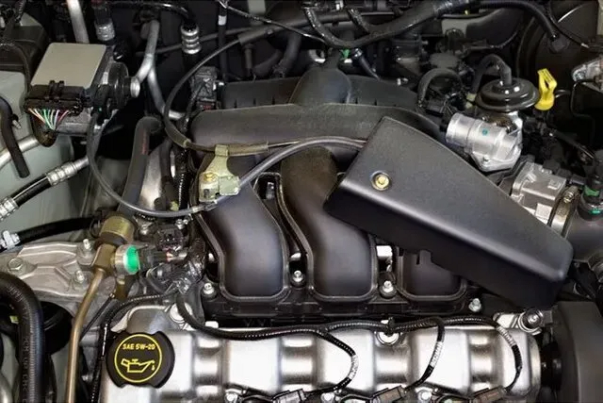 Car engine bay with black intake manifold and silver valve cover, viewed from above