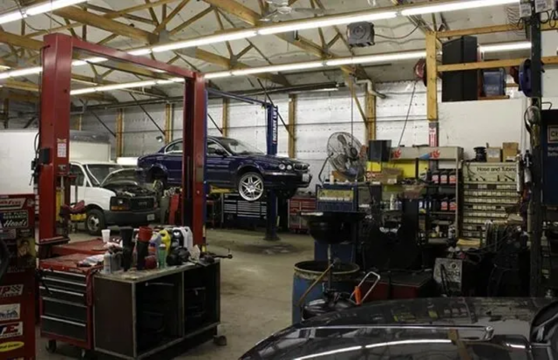 Auto repair shop with a black car on a lift, tools, equipment, and a mechanic working in the background