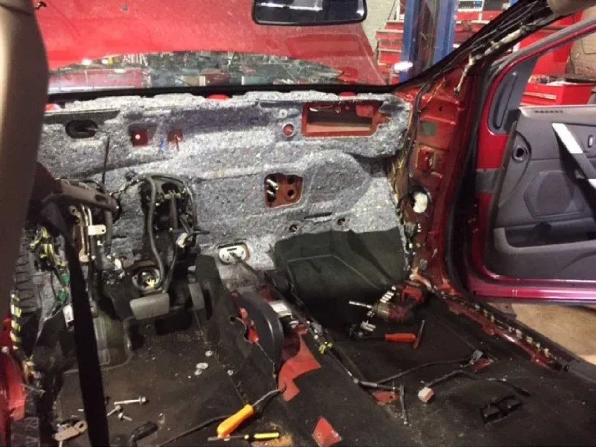 Stripped red car interior with exposed wiring, bare metal, and removed seats during repair.