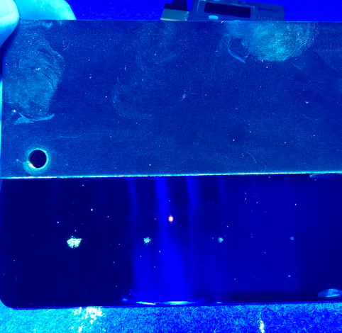 A close-up of a dark, reflective rectangular object with a small circular hole, illuminated by bright blue light.
