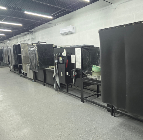 A row of black metal welding stations with dark privacy curtains in an indoor workspace with concrete floors and walls.