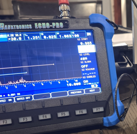 A Danatronics Echo-Pro ultrasonic thickness gauge displaying measurement data on its screen.