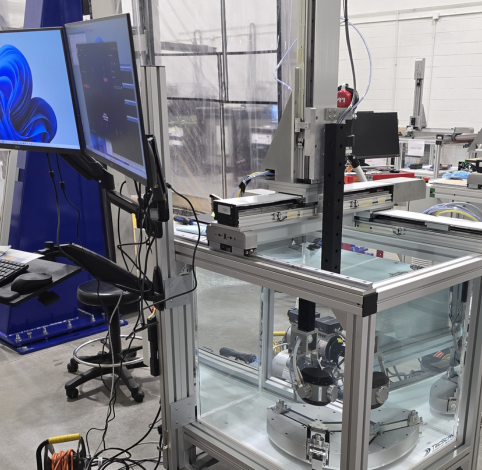 A laboratory workspace with dual computer monitors on an adjustable arm next to a motorized robotic testing enclosure.