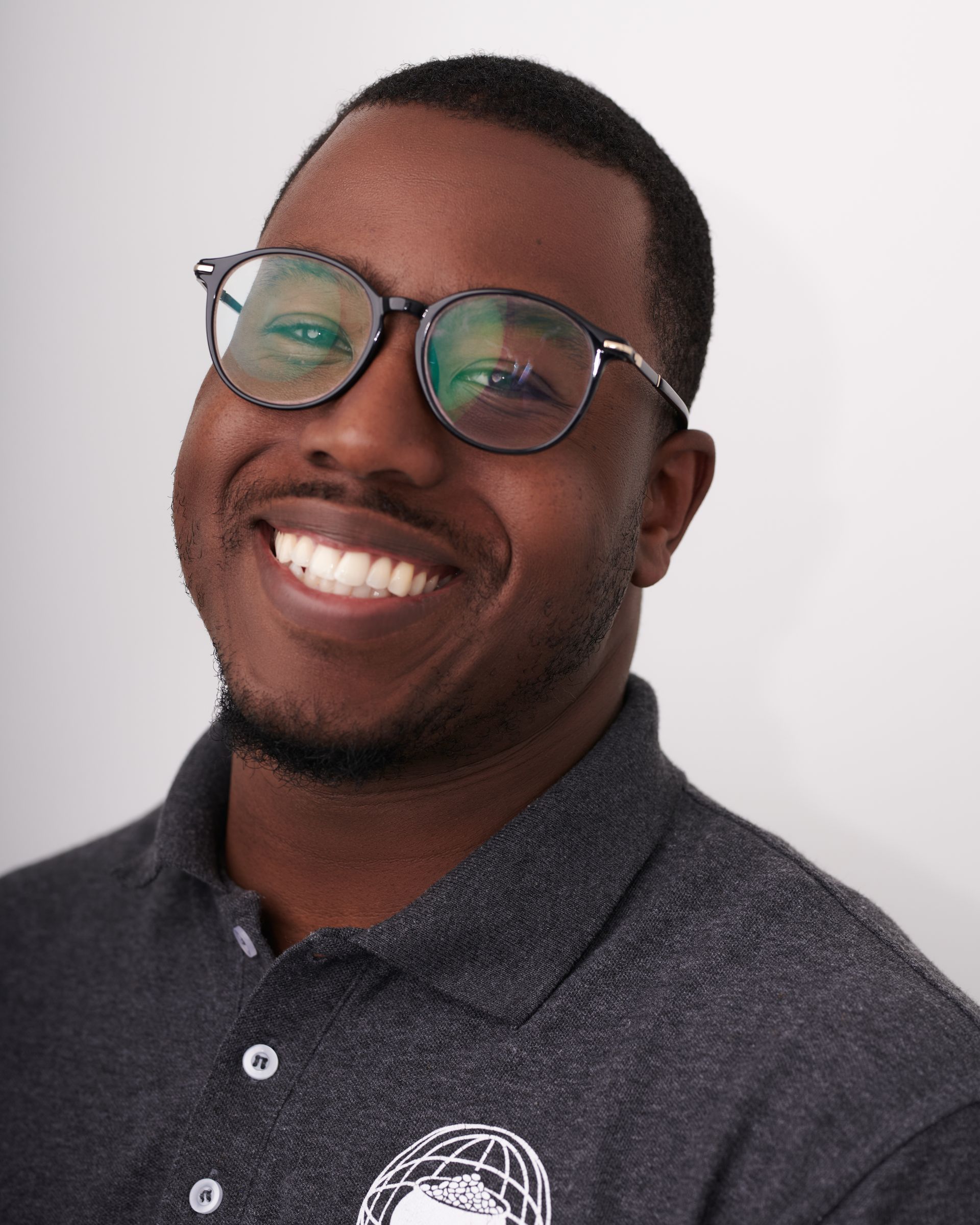 Personne souriante portant des lunettes et un polo gris foncé sur fond clair