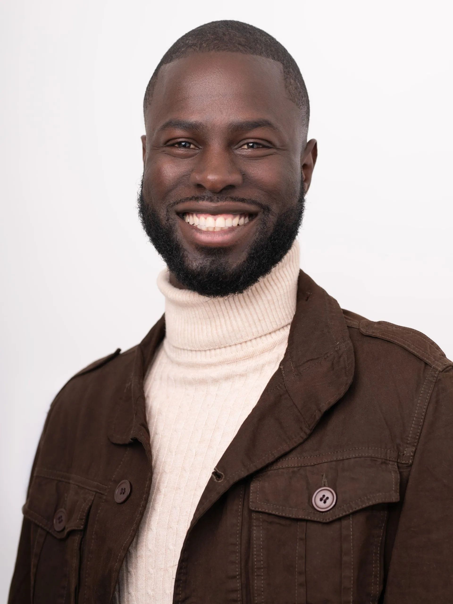 Homme souriant en veste marron et col roulé crème sur fond blanc