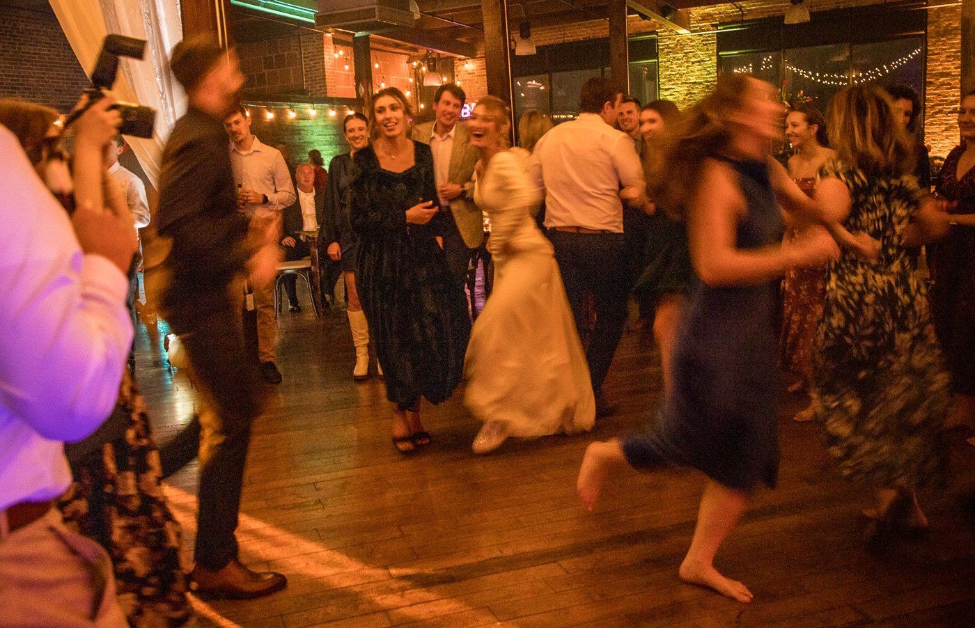 The bride and wedding guests laughing and dancing on a crowded dance floor.