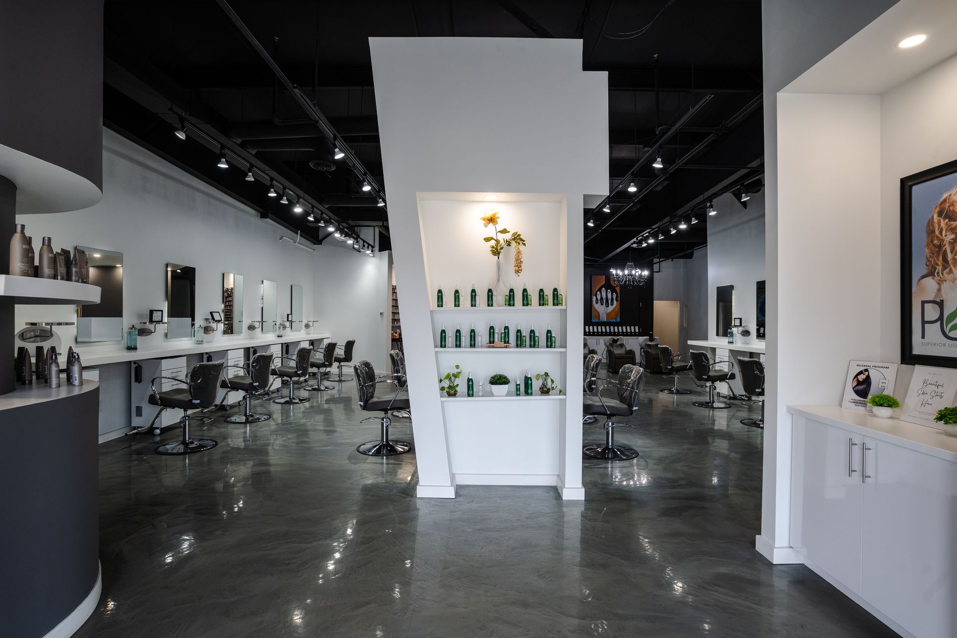 Interior of a modern hair salon with stations, dark ceiling, white walls, and polished concrete floors.