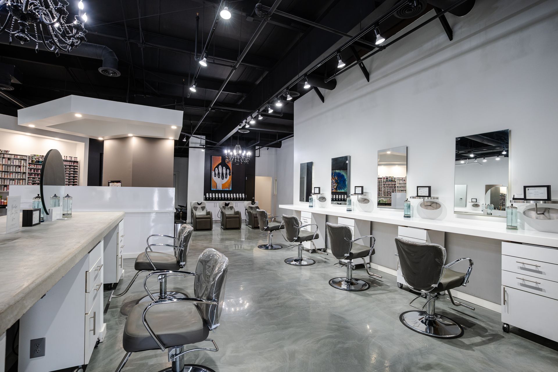 Hair salon interior with styling stations, mirrors, and chairs. White walls and counters, dark ceiling.