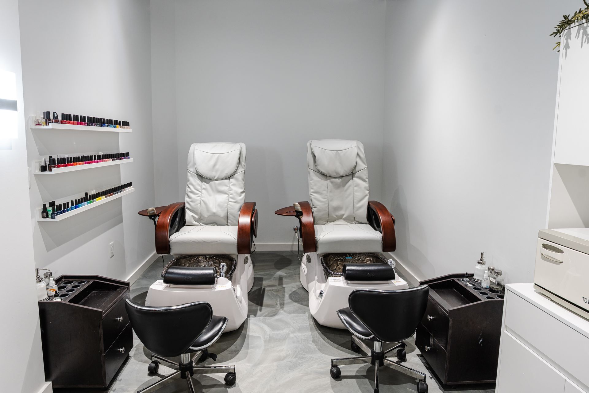 Two pedicure chairs in a salon with nail polish shelves and foot spas.